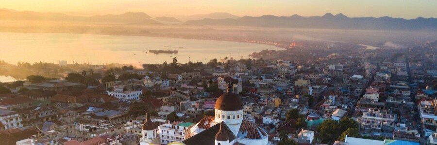Golden sunset over Cap-Haïtien, its cathedral, city streets, waterfront bay, and surrounding mountains in northern Haiti.