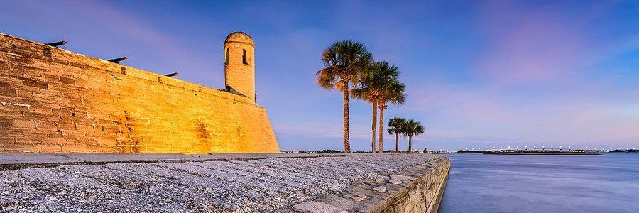 Castillo de San Marcos overlooking Matanzas Bay in St Augustine, Florida, with historic stone walls and palm trees at sunset.