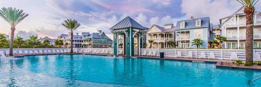 Large resort-style swimming pool surrounded by colorful coastal cottages at Cinnamon Shore in Port Aransas, Texas.