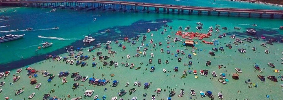 Aerial view of Crab Island in Destin Florida with boats anchored in shallow emerald water near the bridge