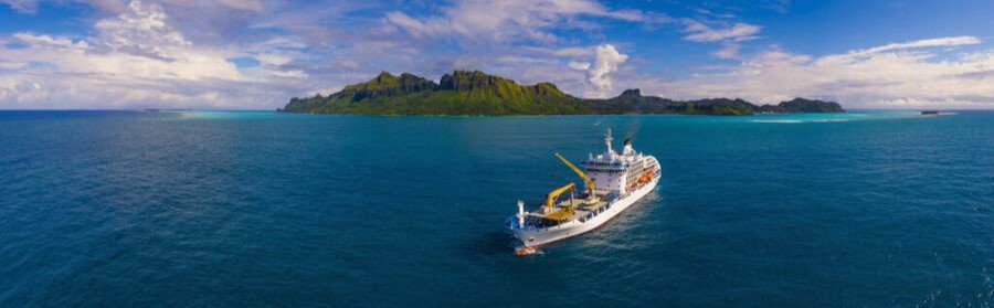 Cruise ship sailing toward Rimatara island with lush green mountains and turquoise ocean in the Austral Islands
