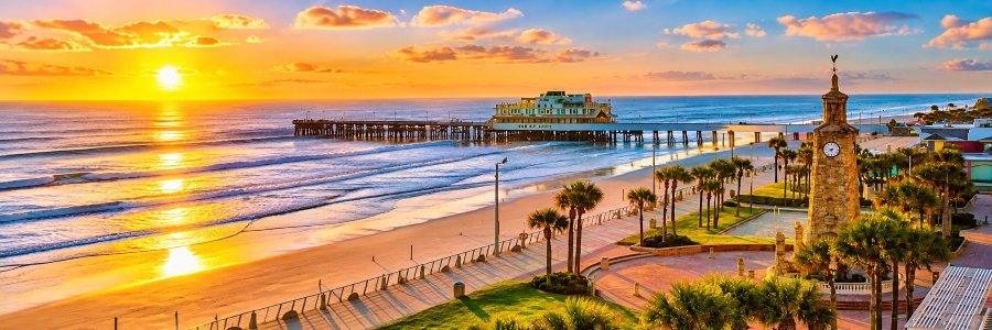 Sunrise over Daytona Beach, Florida, with Atlantic Ocean waves, the beachfront clock tower, and the pier.