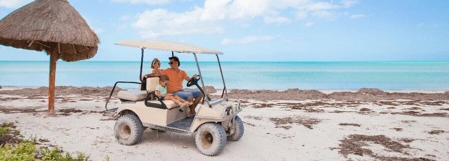 Family riding a street-legal golf cart along a white sand beach in Destin Florida