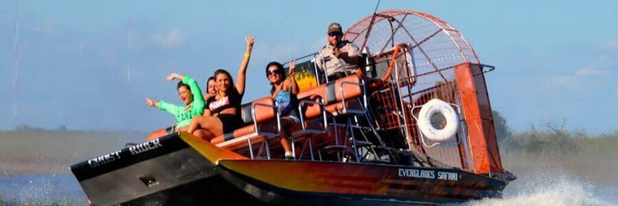 A large Everglades Safari Park airboat named Ghost Rider speeding through wetland waters with excited tourists and a driver.