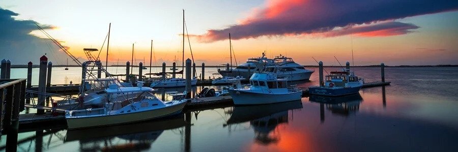 Several motorboats and yachts docked at a tranquil marina under a dramatic orange and purple sunset sky on Florida's First Coast.