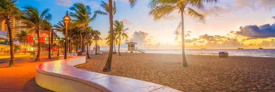 Fort Lauderdale Beach promenade lined with palm trees during a colorful sunset over the Atlantic Ocean.