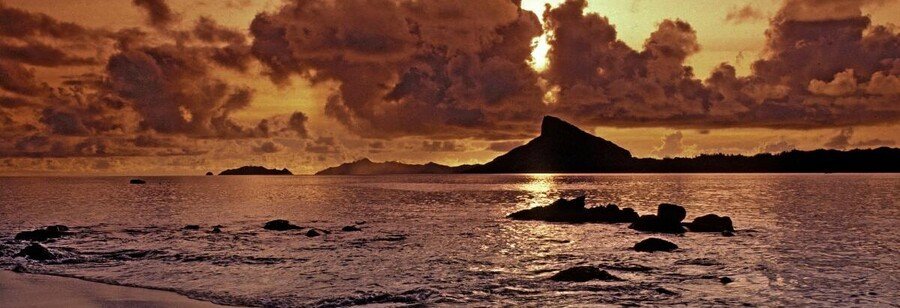 Sunset over the Gambier Islands lagoon with calm water, clouds, and island silhouette