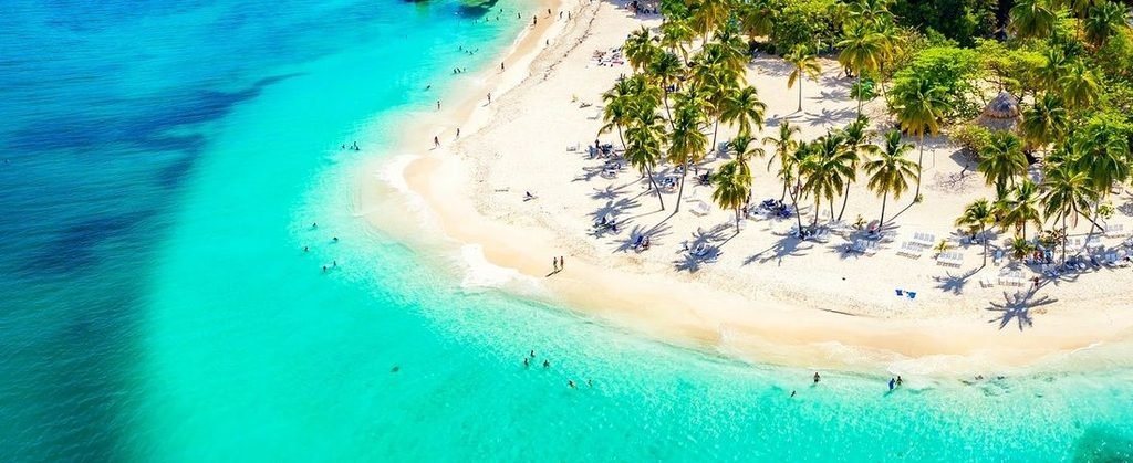 Aerial view of a beautiful Caribbean beach with turquoise water, white sand, lush tropical greenery, and palm trees in the Greater Antilles.