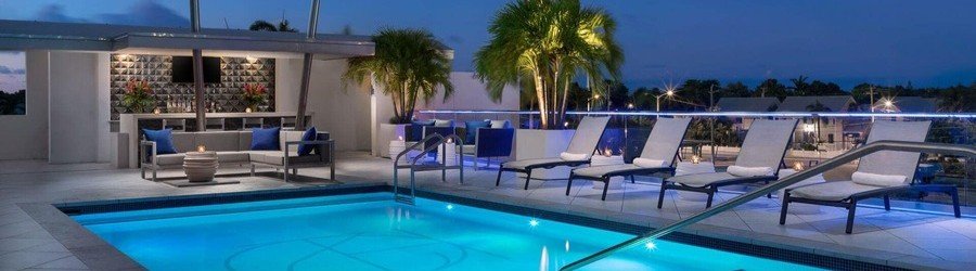 Luxury rooftop pool at H2O Suites Hotel in Key West with palm trees, lounge chairs, and relaxing evening lighting.