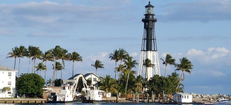 Hillsboro Inlet Lighthouse surrounded by palm trees and boats along the Intracoastal Waterway in Pompano Beach.