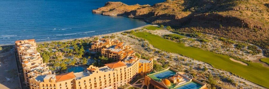 hotel-loreto-palmar-pool-ocean-view | Beach Travel Destinations Hotel Loreto Palmar in Loreto, Mexico featuring a resort-style pool surrounded by palm trees, lounge chairs, and shaded umbrellas with views of the Sea of Cortez in the background
