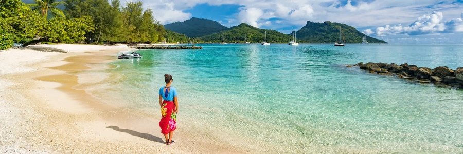 Huahine beach with clear turquoise lagoon, palm trees, and lush green mountains in French Polynesia