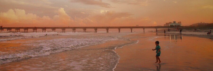 Jacksonville Beach at sunset with colorful skies, gentle waves, and visitors enjoying the shoreline near the pier.