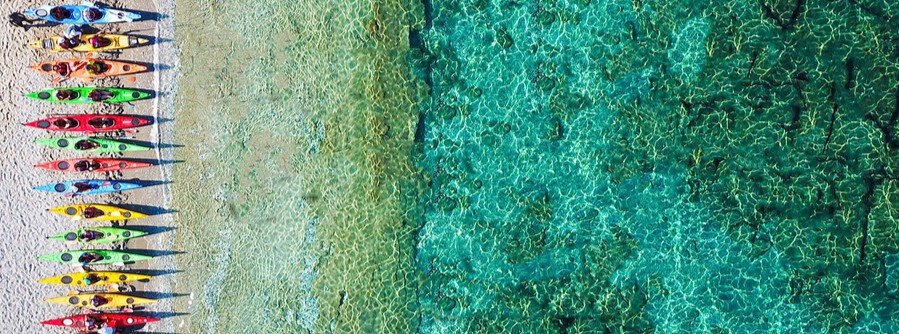 Colorful kayaks lined up on a Skopelos beach next to crystal-clear turquoise water viewed from above