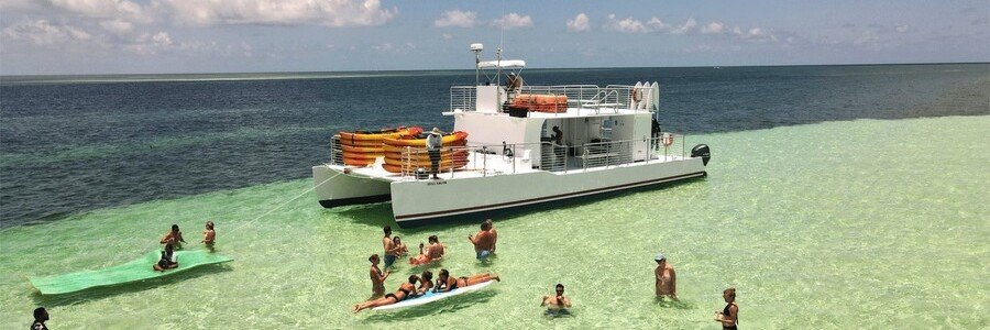 Catamaran anchored at a shallow Key West sandbar with people relaxing in clear turquoise water under a sunny sky.