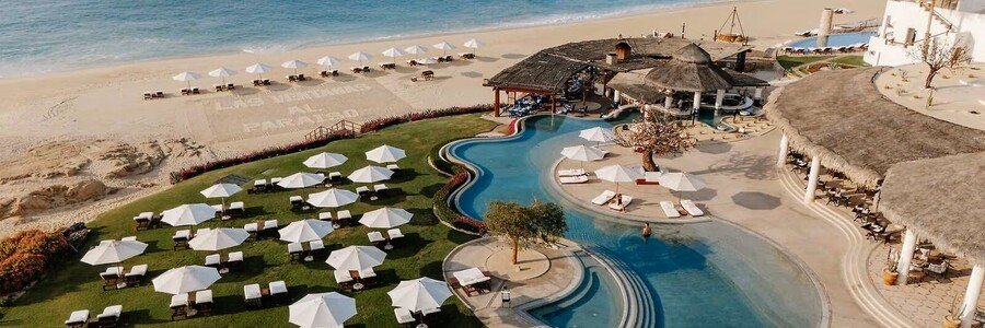 Curved swimming pool, white umbrellas and beachfront lawn at Las Ventanas al Paraíso, a Rosewood Resort.