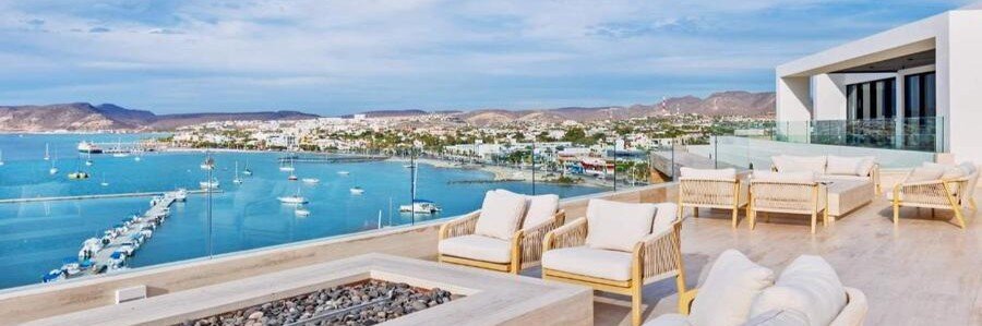 Luxury ocean-view terrace at Live Aqua Private Residences La Paz featuring modern outdoor seating, a fire pit, and panoramic views of the marina, boats, and the Sea of Cortez coastline.