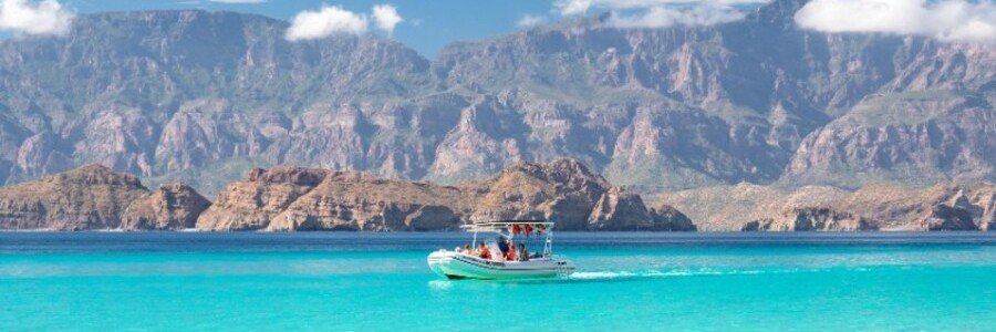 loreto-carmen-island-boat-tour-snorkeling-sea-of-cortez | Beach Travel Destinations Small boat on turquoise water near Carmen Island in Loreto, Mexico, with mountains in the background and clear Sea of Cortez ideal for snorkeling tours