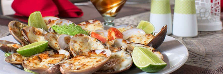 loreto-chocolate-clams-grilled-seafood-local-dish | Beach Travel Destinations Plate of grilled chocolate clams served with lime wedges and garnish in Loreto, Mexico, a popular local seafood dish from the Sea of Cortez