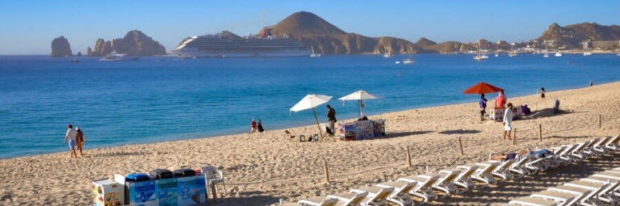 Cabo Beaches at Médano Beach with lounge chairs, calm water, boats, and Land’s End views