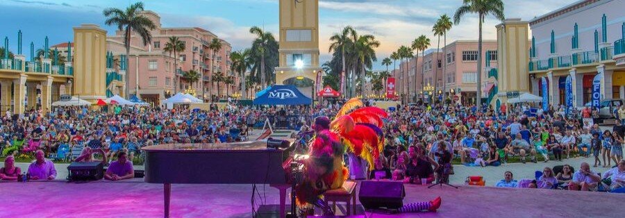 Live outdoor event at Mizner Park Boca Raton Florida with crowd, stage performance, palm trees, and evening city atmosphere