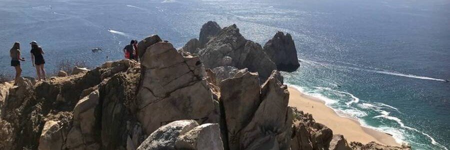 Hikers standing on the rocky summit of Mount Solmar above Land’s End, the Pacific shoreline and deep blue water.