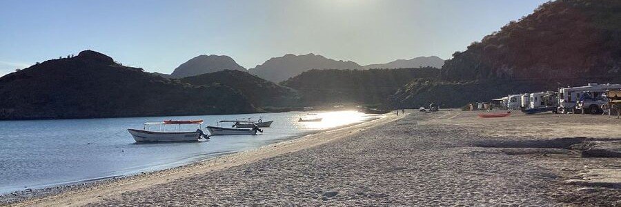 Quiet beach near Mulegé, Mexico, with small boats resting on calm water and soft sand along the shoreline