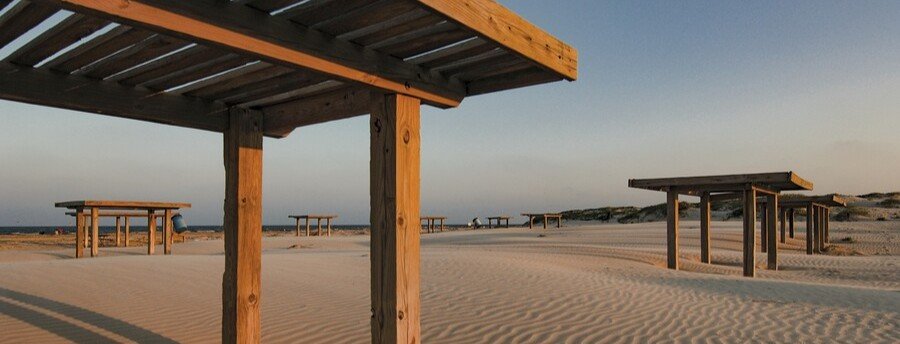 Wooden shade shelters on sandy dunes at Mustang Island State Park beach camping area in Texas.