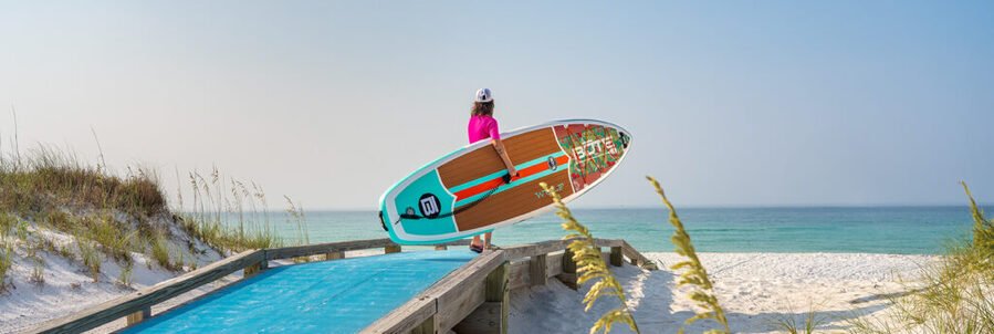 Person carrying paddleboard toward Navarre Beach Florida with white sand dunes and Gulf Coast water