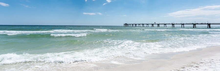 Okaloosa Island beach in Fort Walton Beach Florida with white sand, emerald waves, and fishing pier