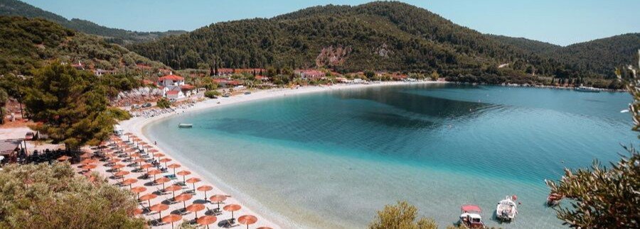 Panormos Beach with calm turquoise bay and sunbeds along the shoreline on Skopelos Island
