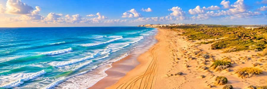 Panoramic view of Playa de Matas Blancas in Fuerteventura, featuring a long golden sandy shoreline, turquoise Atlantic waves, coastal dunes, and open ocean views.