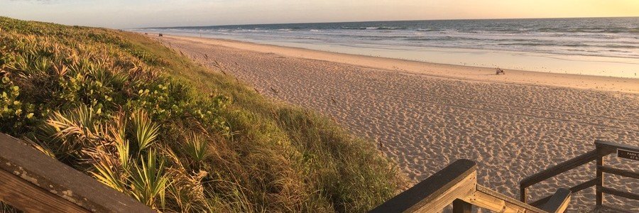 Wooden boardwalk stairs leading down to the wide uncrowded sands and pristine dunes of Playalinda Beach at Canaveral National Seashore.
