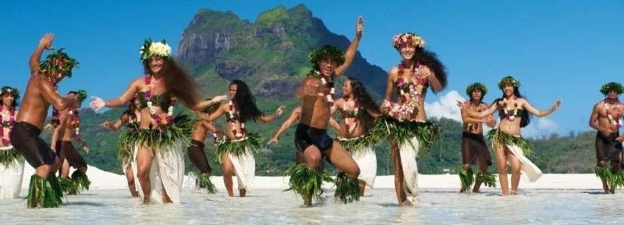 Polynesian dancers performing in shallow lagoon with mountain backdrop