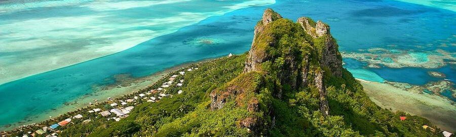 Aerial view of Raiatea mountain peak with lush greenery overlooking turquoise lagoon in French Polynesia