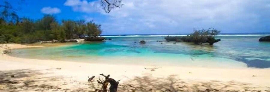 White sand beach and turquoise lagoon with rocky outcrops and tropical trees in Rimatara, Austral Islands