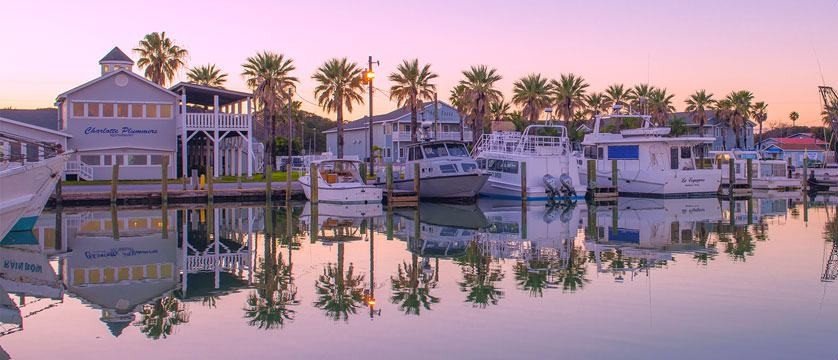 Sunset over Rockport Texas harbor with boats and palm trees reflected on Aransas Bay.