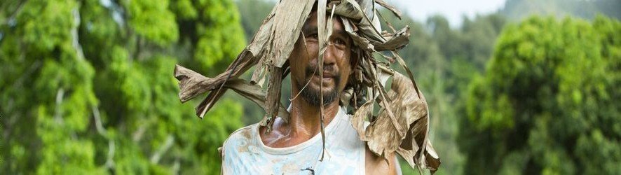 Local coffee farmer in Rurutu standing in lush green fields wearing natural leaf hat in the Austral Islands