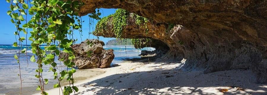Natural rock arch and cave on a sandy beach in Rurutu with ocean view and hanging green vines