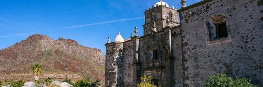 san-javier-mission-loreto-historic-desert-landmark | Beach Travel Destinations San Javier Mission near Loreto, Mexico, a historic stone church set against desert mountains with clear blue sky and surrounding rugged landscape