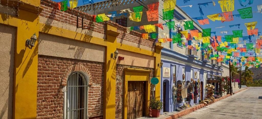 A vibrant cobblestone street in San Jose del Cabo lined with historic brick buildings and colorful hanging banners.