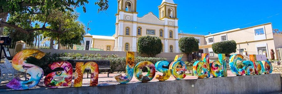 Colorful San José del Cabo sign in front of a historic church plaza with bright artwork and sunny Baja skies.