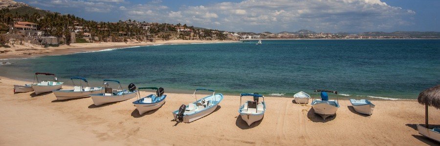A row of white and blue fishing boats parked on the golden sand of Palmilla Beach in San Jose del Cabo.
