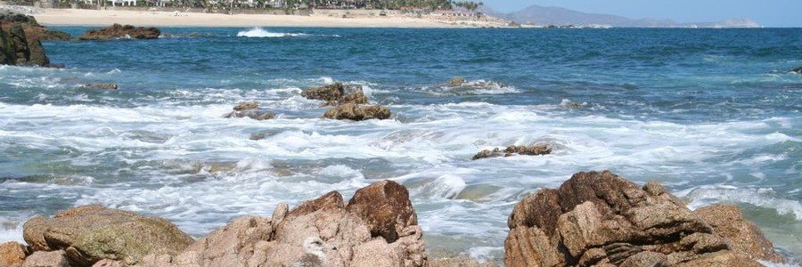 Rocky shoreline in San José del Cabo with crashing ocean waves, coastal scenery, and bright blue water along the Baja coast.