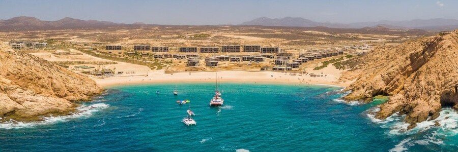 Aerial view of Cabo Beaches at Santa Maria Bay with turquoise water, boats, golden cliffs, and a curved beach