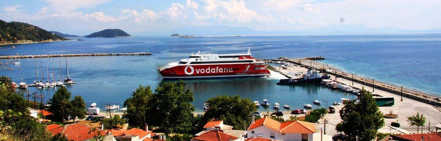 Ferry arriving at Skopelos port in the Aegean Sea with boats, turquoise water, and coastal village views
