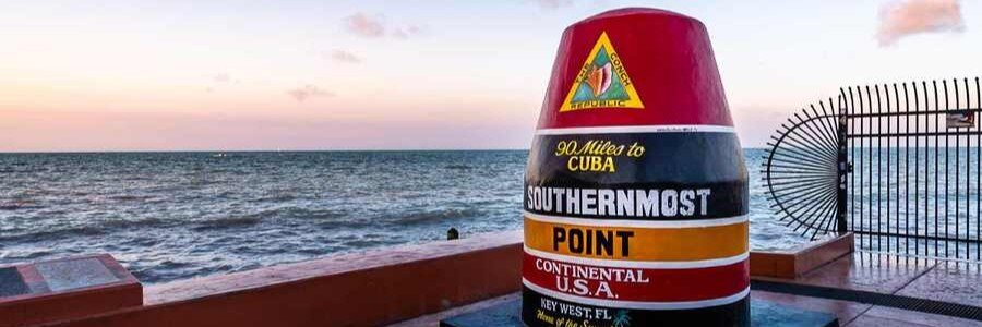 The iconic colorful painted concrete Southernmost Point Buoy monument standing along the ocean shoreline in Key West during twilight.