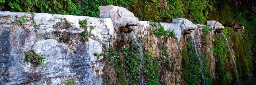 Stone lion-head fountains flowing with spring water in Menites on Andros Island, Greece.