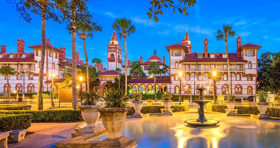 Historic Flagler College illuminated at dusk in St Augustine, Florida, surrounded by palm trees and Spanish Renaissance architecture.