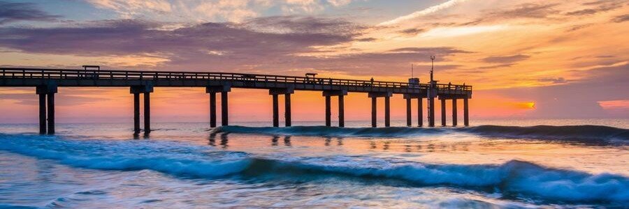 Sunset over St Augustine Beach Pier with colorful skies and ocean waves along Florida's coast.
